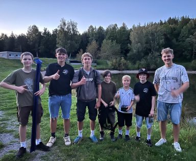 Gruppe von sieben Jugendlichen am Ufer eines Gewässers, lächelnd und posierend.