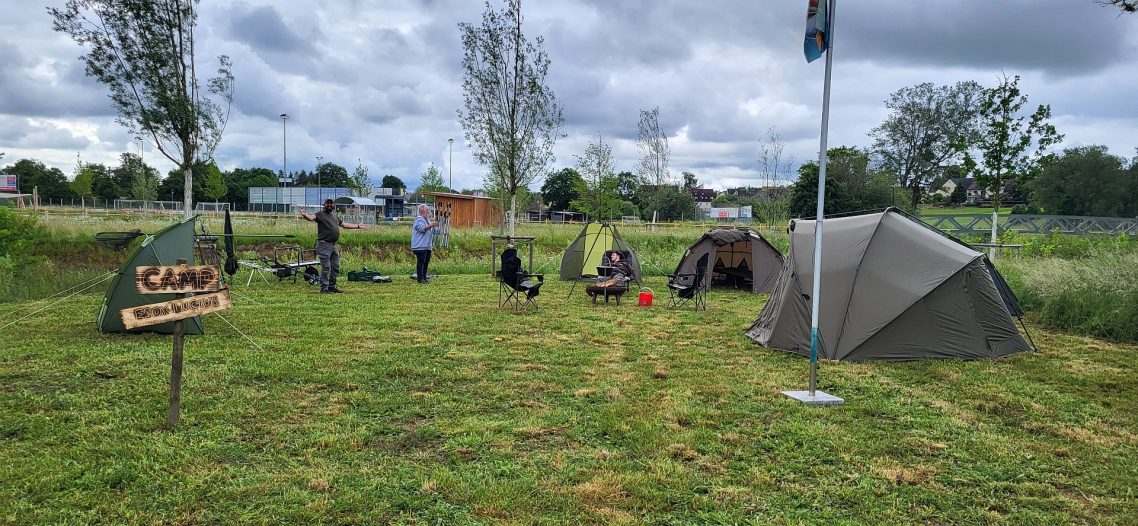 Das Camp ist vorbereitet! Campingplatz mit mehreren Zelten und Personen in einer grünen Umgebung.