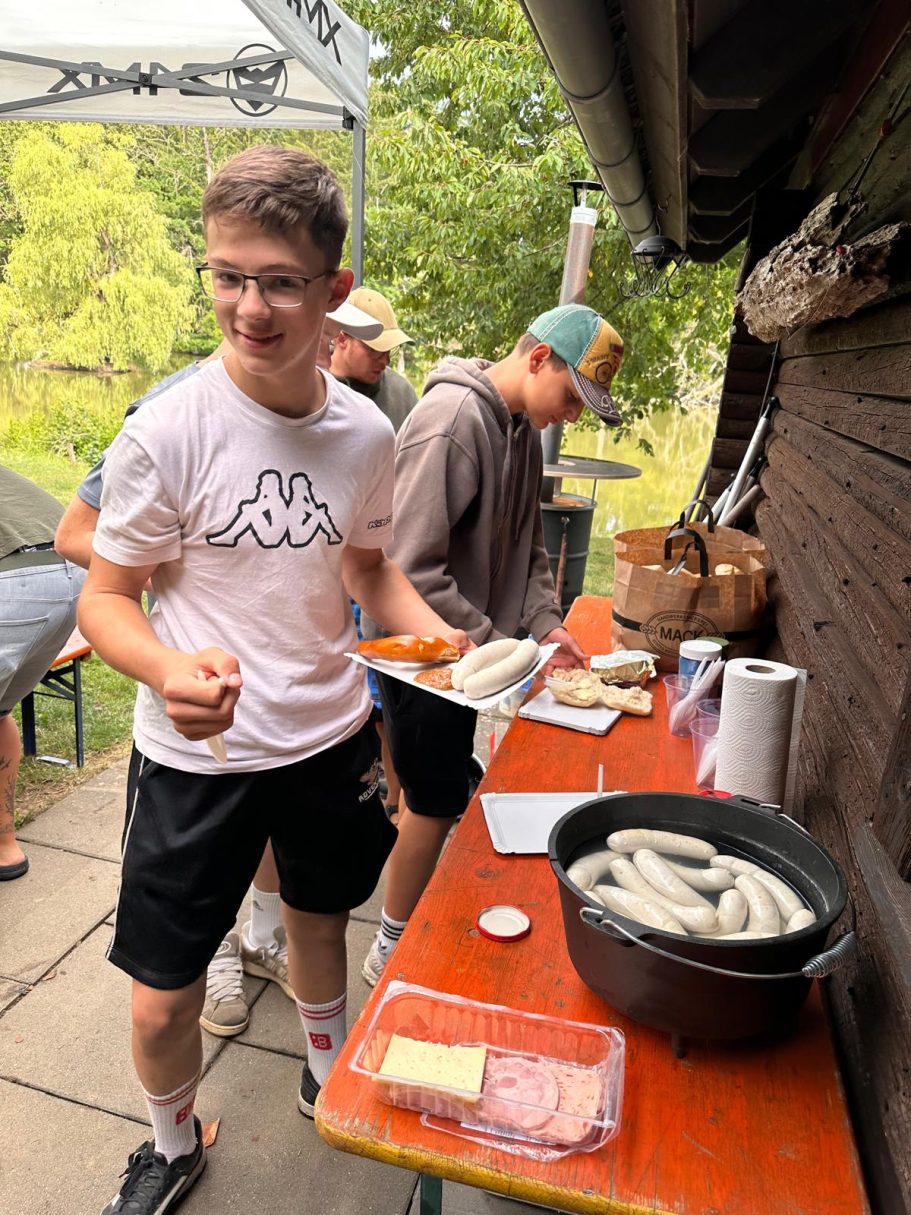 Gemeinsam feiern Junge bereitet Würstchen auf einem Tisch im Freien vor, im Hintergrund Bäume.
