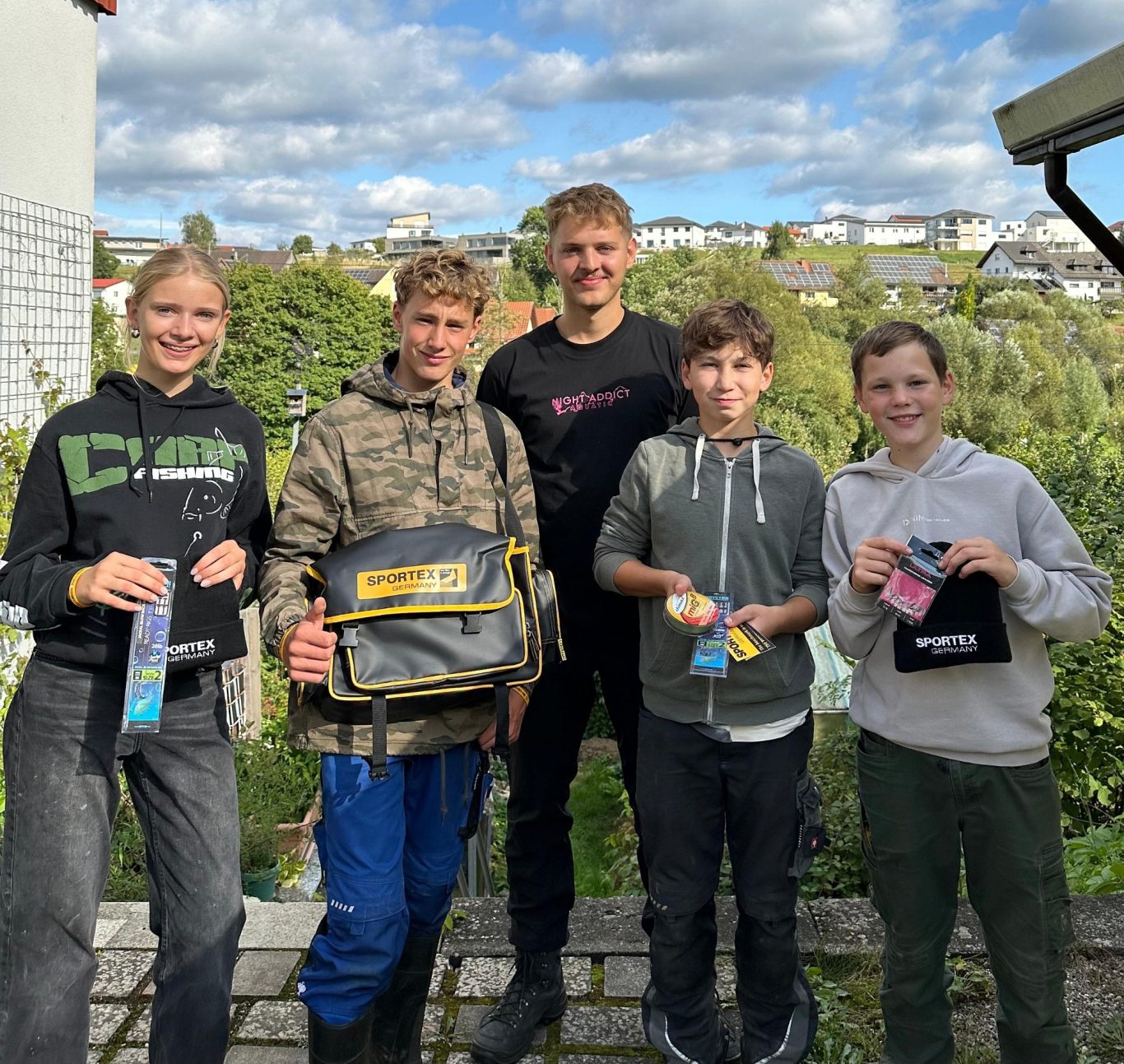 Unsere Jugend in Aktion Fünf Personen stehen im Freien und halten verschiedene Gegenstände in den Händen.