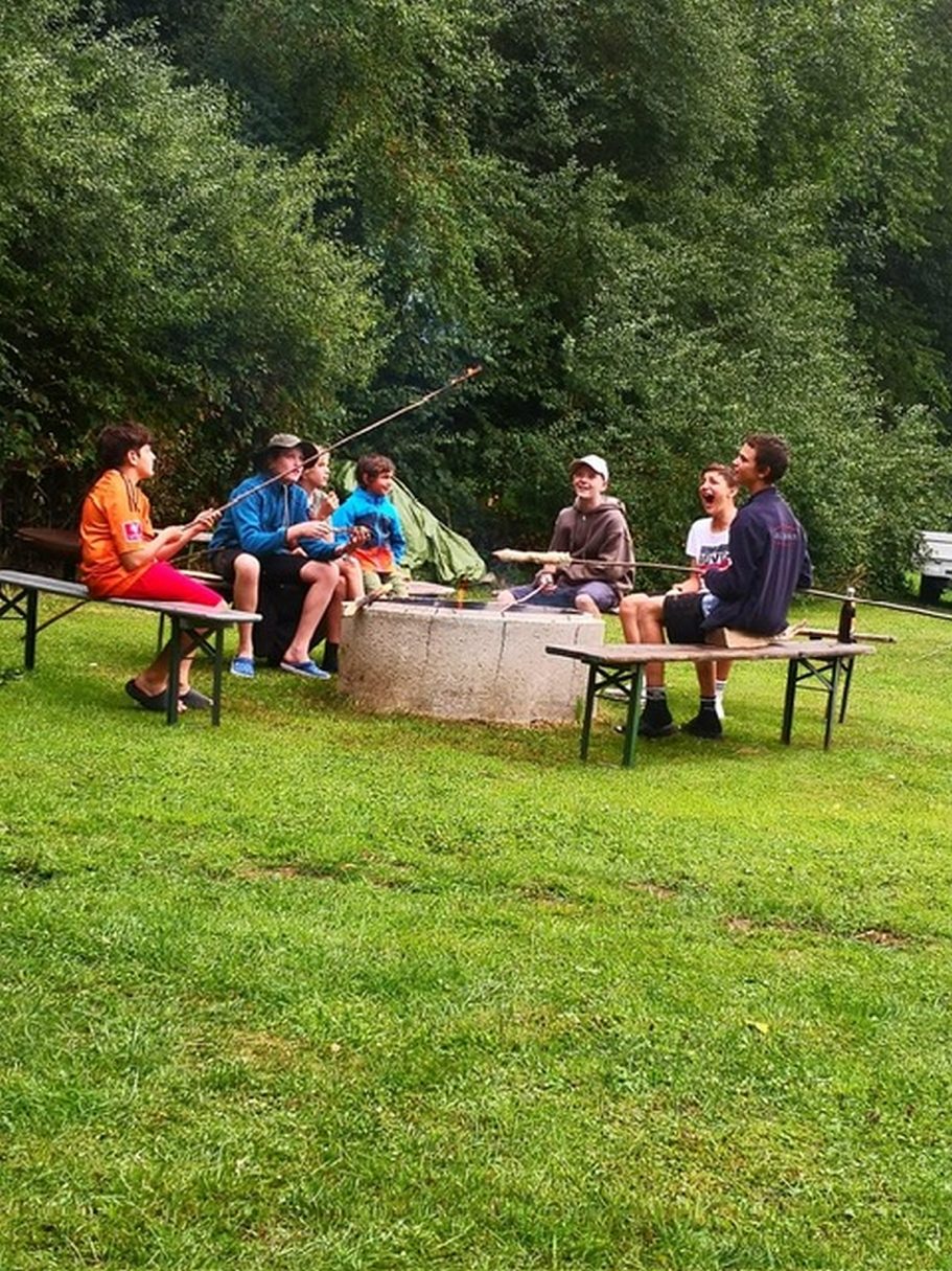 Gemeinsam feiern Gruppe von Menschen sitzt um ein Feuer auf Bänken in einer grünen Landschaft.