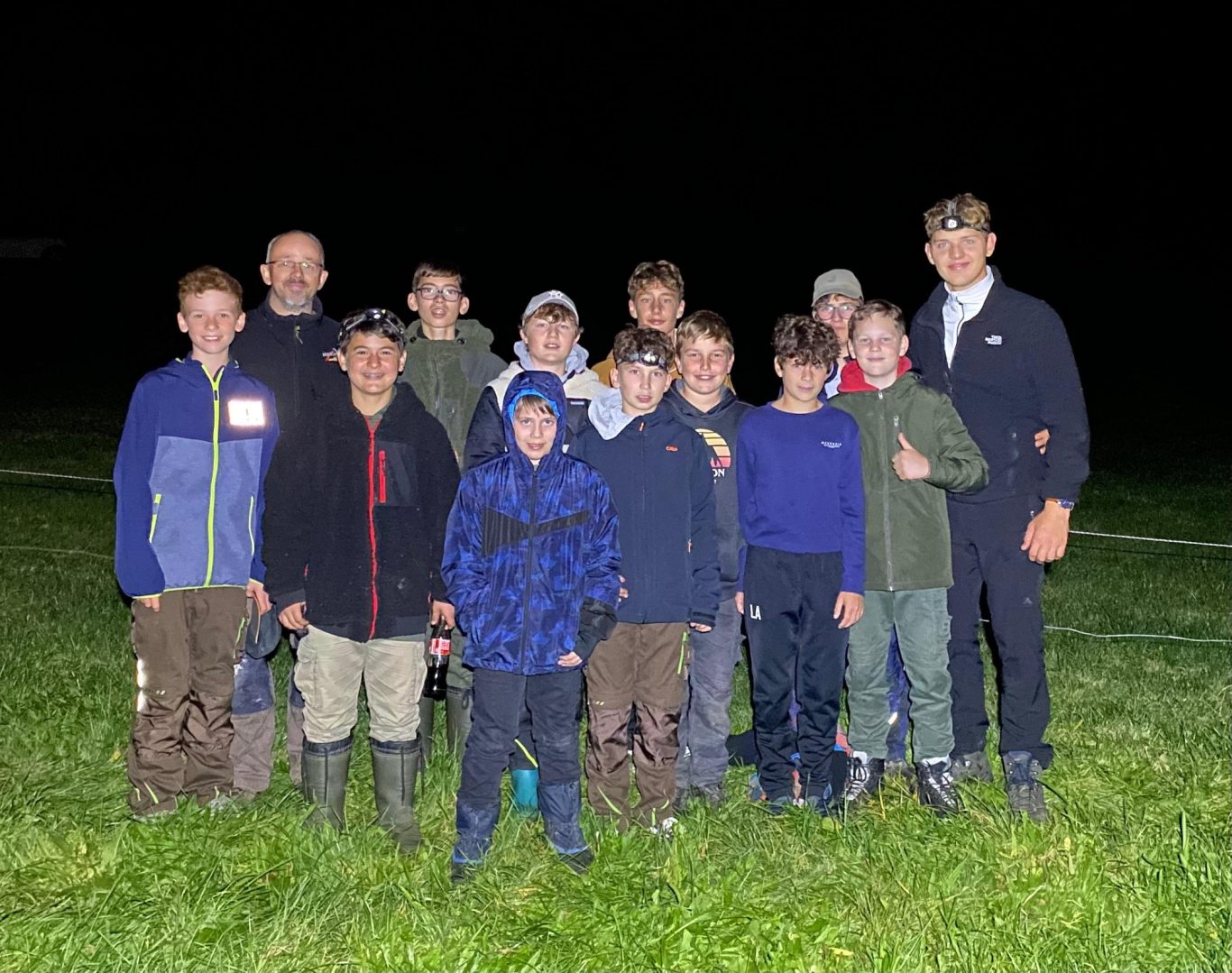 Unsere Jugend in Aktion Gruppe von Jungen und Erwachsenen bei Nacht im Freien, umgeben von Gras.