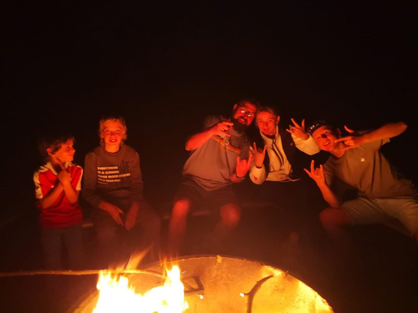 Gruppe von fünf Personen um ein Lagerfeuer, lächelnd und posierend.