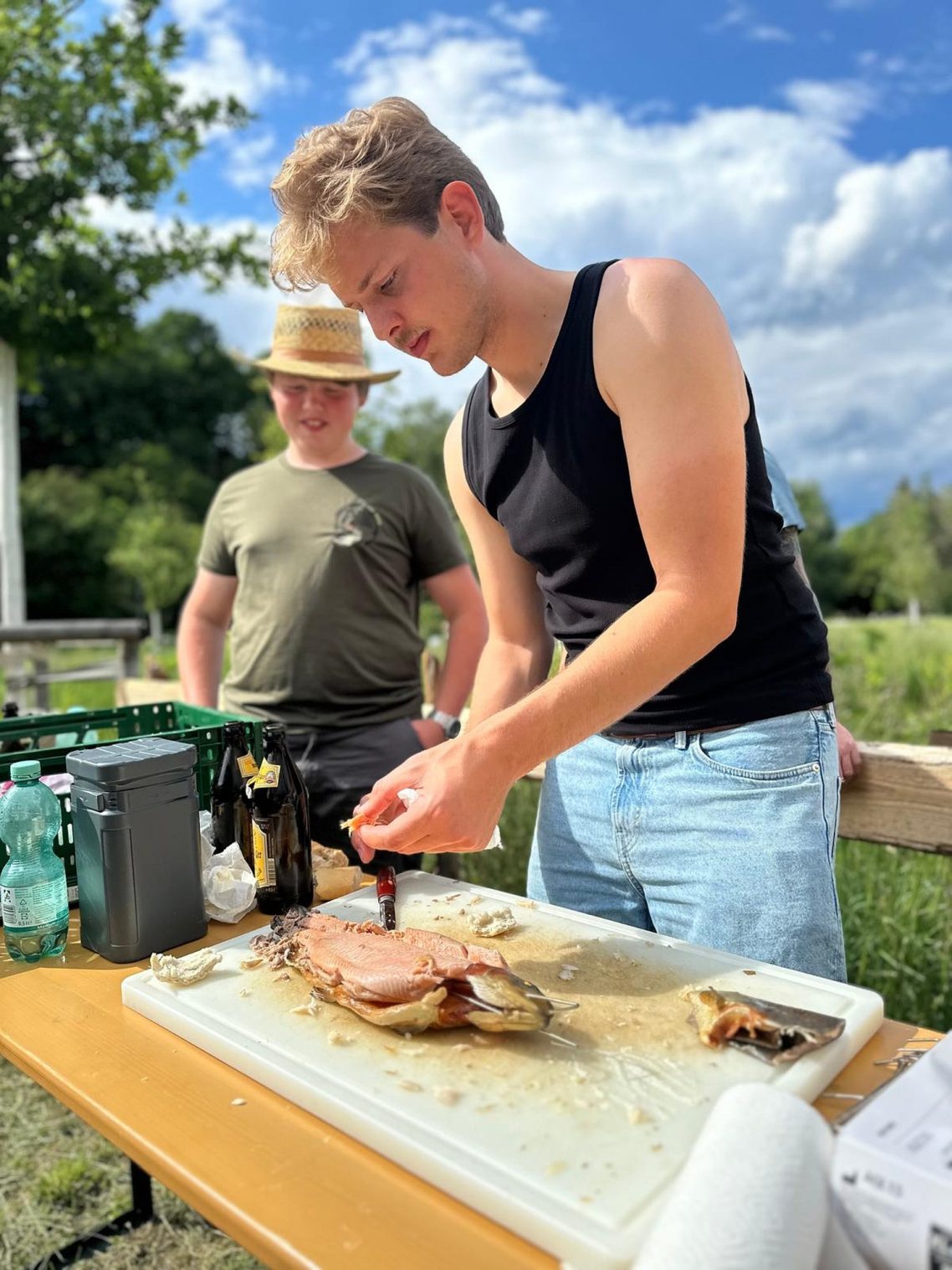 Zeigen ist wichtig Junger Mann schneidet Fleisch an einem Tisch; ein zweiter Mann im Hintergrund schaut zu.