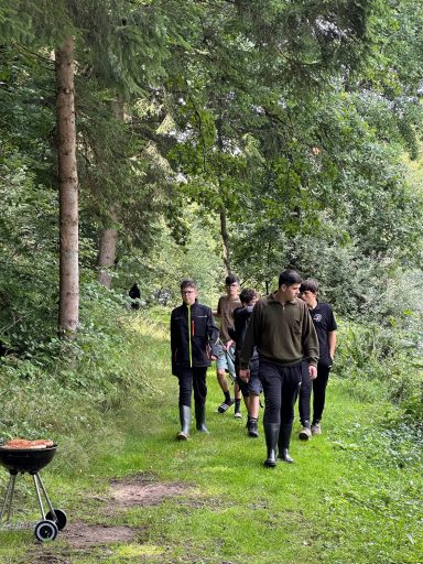Gruppe von Menschen, die einen Waldweg entlanggehen, neben einem Grill.