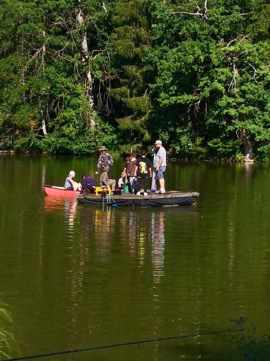 Gruppen von Menschen stehen und sitzen auf einem kleinen Boot auf einem ruhigen See.