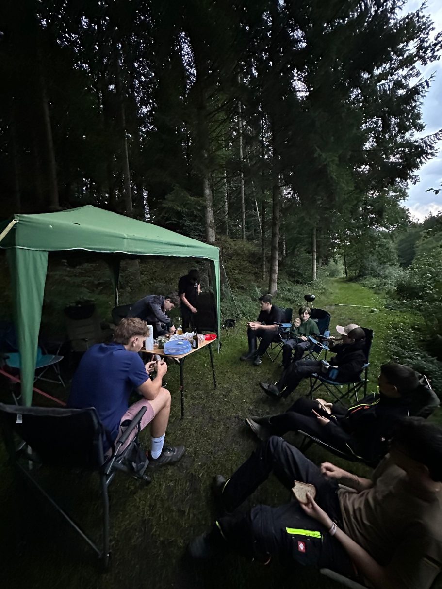 Schulung Gruppe von Personen sitzt unter einem grünen Pavillon im Wald.