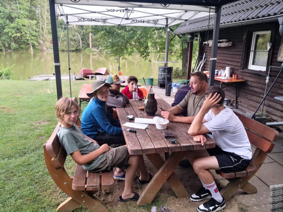Schulung Sechs Personen sitzen an einem Tisch unter einem Pavillon am Wasser.