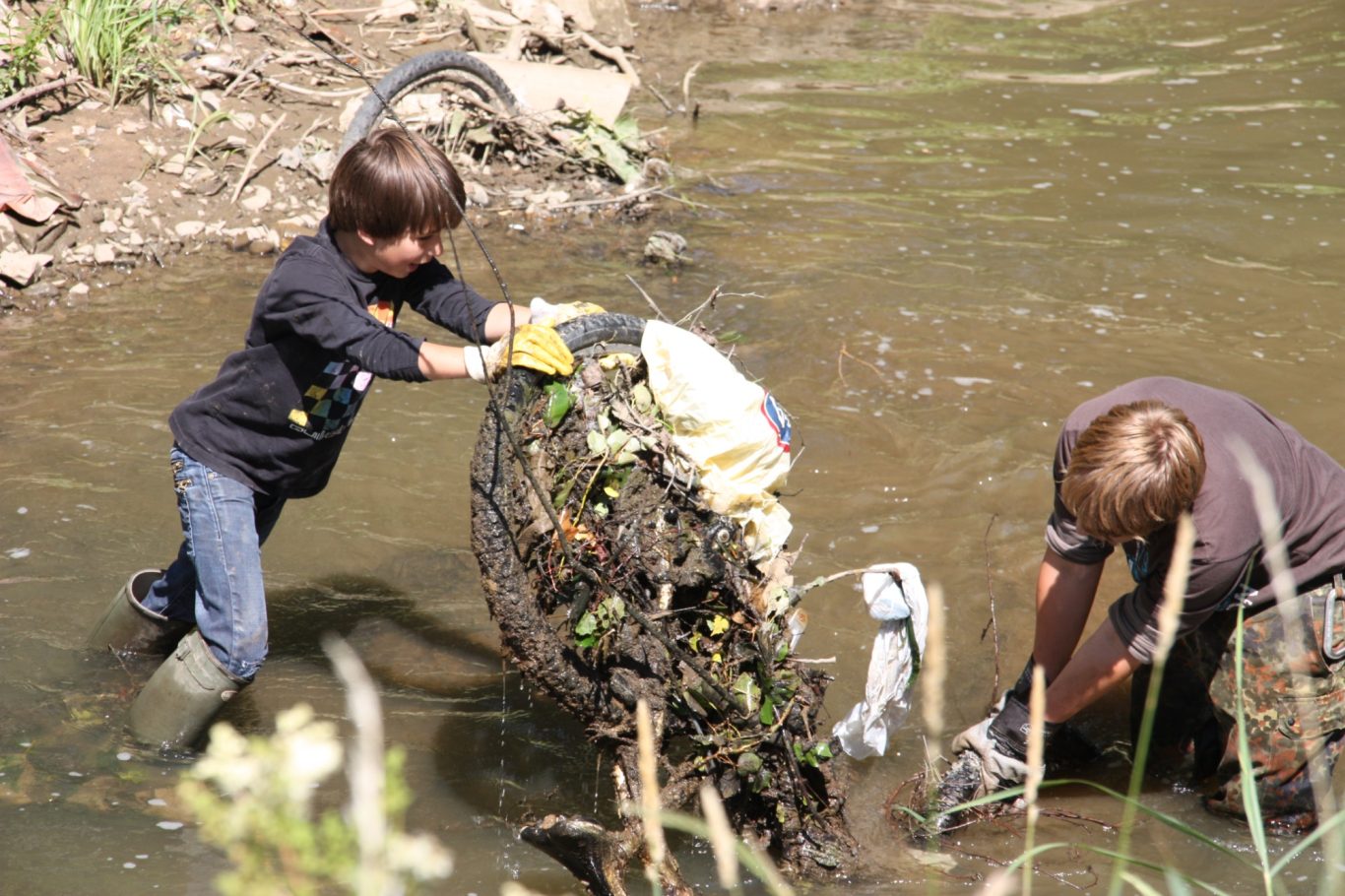 Gewässerreinigung Zwei Kinder reinigen einen verschmutzten Gewässerbereich von Müll und Abfällen.