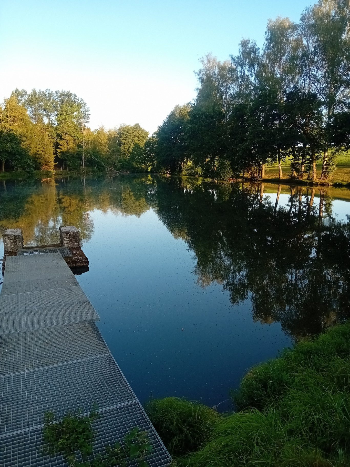 Ruhiger See mit Spiegelung der Bäume und einem Steg im Vordergrund. Ruhiger See mit Spiegelung der Bäume und einem Steg im Vordergrund.