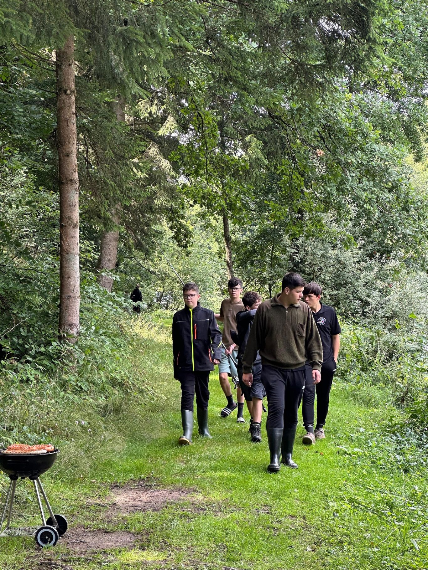 Unsere Jugend in Aktion Gruppe von Menschen, die auf einem Waldweg gehen, während ein Grill im Vordergrund steht.