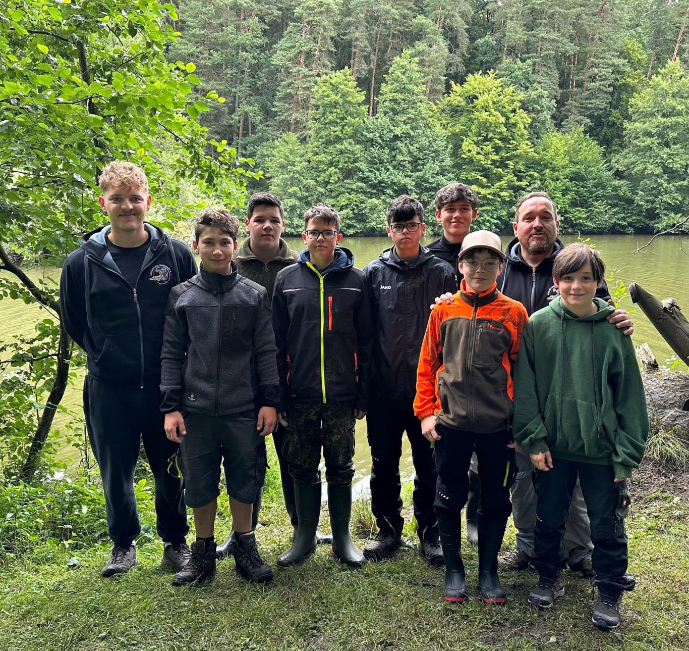 Unsere Jugend in Aktion Gruppe von acht Personen am Ufer eines Gewässers, umgeben von Bäumen.