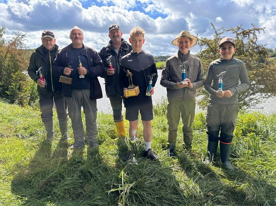 Wettkampf Sechs Personen stehen am Ufer eines Gewässers, halten Tropfenflaschen und lächeln.